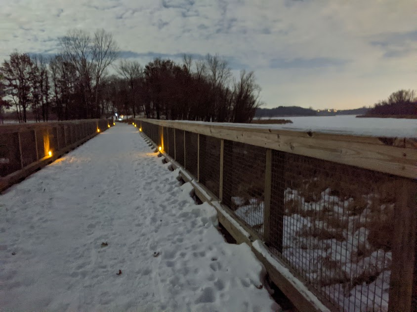 photo of snow covered trail bridge with candles at dusk